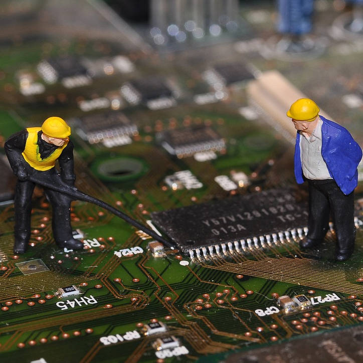 Photo of electronic circuit board with two mini plastic figures of construction workers standing on it